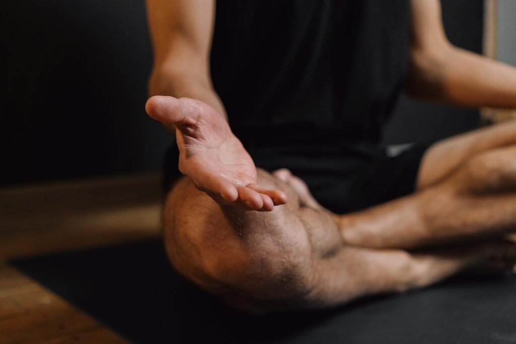 Crop unrecognizable barefoot male sitting with crossed legs on sports mat during stress relief meditation session